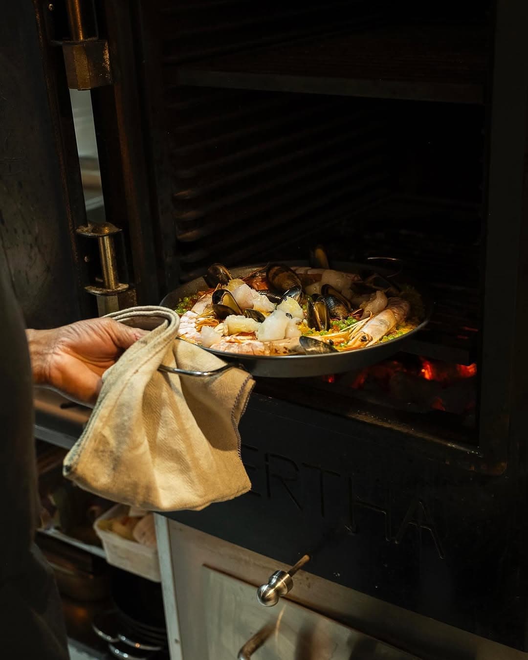 A seafood paella pulled from the Bertha oven, its door embossed BERTHA.