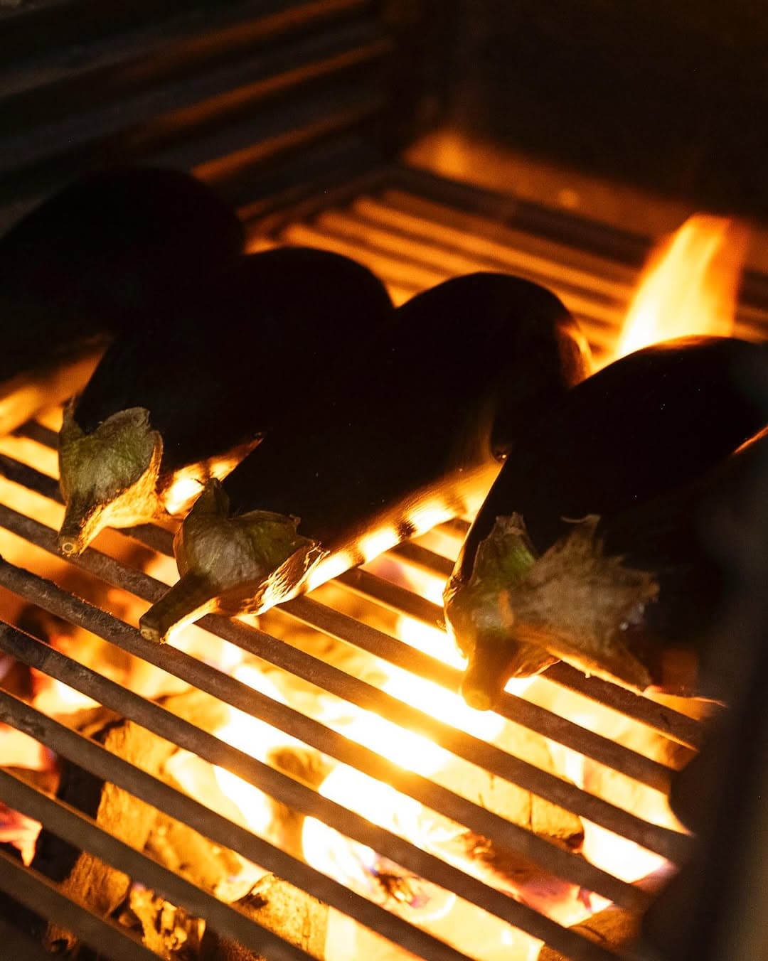 Charcoal aubergines roasting over an open flame.