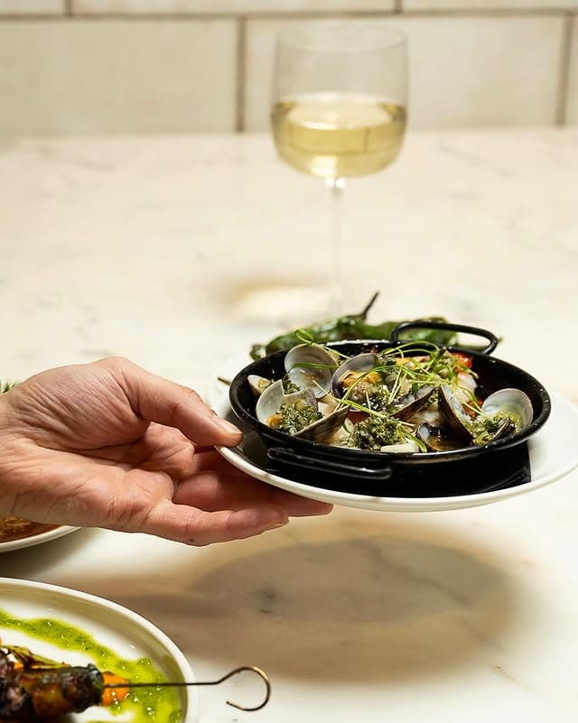 Clams in a black pan on marble against the white-tiled counter wall.