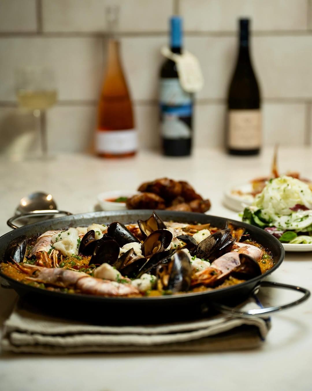 Seafood paella with wine against the white-tiled counter wall.